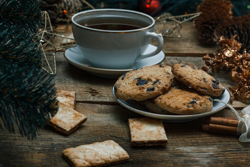Beautiful concept. Chocolate cookies on a white plate on a wooden background. Nearby stands a Christmas tree, toys, tea, garlands and Christmas toys.