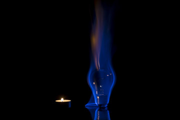 Small candle and tungsten light bulb burning with a beautiful blue flame