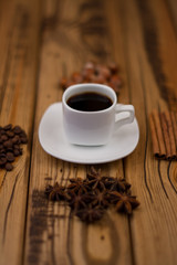 Small white cup of coffee, cinnamon sticks, cocoa beans, star anise, hazelnuts on wooden background