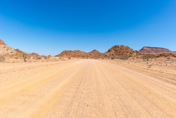 Fototapeta na wymiar Gravel 4x4 road crossing the colorful desert at Twyfelfontein, in the majestic Damaraland Brandberg, scenic travel destination in Namibia, Africa.