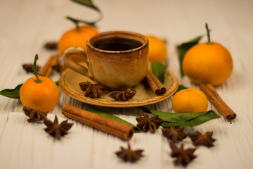 Small white cup of coffee, cinnamon sticks, star anise and mandarin on white wooden background