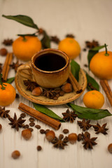 Small cup of coffee, cinnamon sticks, cocoa beans, star anise, hazelnuts and mandarins on white wooden background
