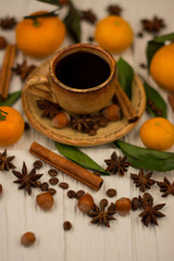 Small cup of coffee, cinnamon sticks, cocoa beans, star anise, hazelnuts and mandarins on white wooden background
