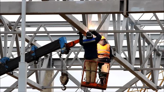 a welder working at height without insurance in a cradle lift in the construction of large shopping complex metal structures and concrete piles.