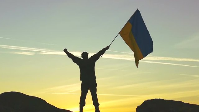 
Silhouette of Soldier with Ukrainian Flag Against orange Sky. Slow Motion 
