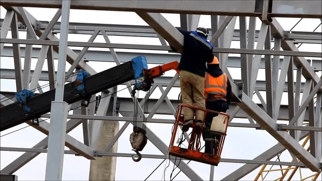 a welder working at height without insurance in a cradle lift in the construction of large shopping complex metal structures and concrete piles.