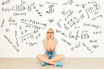 attractive shocked girl in spectacles  sitting on floor near wal