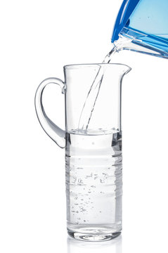 Pouring clear water from filter pitcher in glass jug on white ba