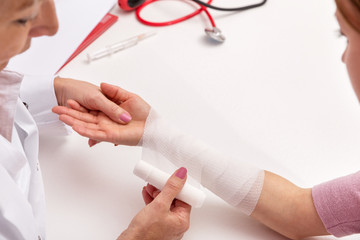 Ärztin legt Verband an, Frau mit verletztem Unterarm