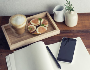 Cappuccino and figs bagel on table with nitebook and cellphone