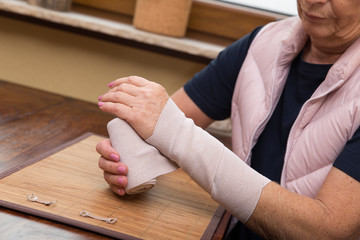 Ältere Frau verbindet sich ihren Arm mit einem Verband selbst
