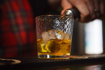 Bartender pours whiskey with ice closeup