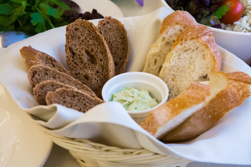 White bread and black bread with greens. Sliced bread on the serving table in a wicker basket with white sauce. The food for Breakfast, lunch and dinner.