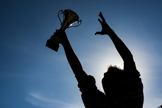 Champion and winning concept. Silhouette of a hand holding a championship trophy against the sky