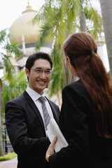 Businessman and businesswoman shaking hands, mosque in the background