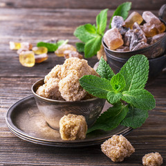 Lump brown cane sugar in a vintage metal dishes with  sprig of fresh mint on  simple wooden background. The concept  natural organic food.
