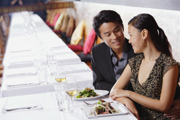 Couple in restaurant, sitting side by side, looking at each other