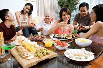 Adults having a party in living room, food on coffee table
