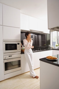 Young woman standing in kitchen, having coffee
