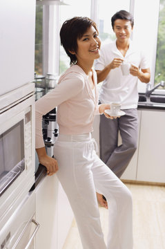 Couple standing in kitchen, having coffee, looking at camera