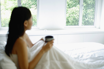 Woman sitting up in bed, holding cup, looking away