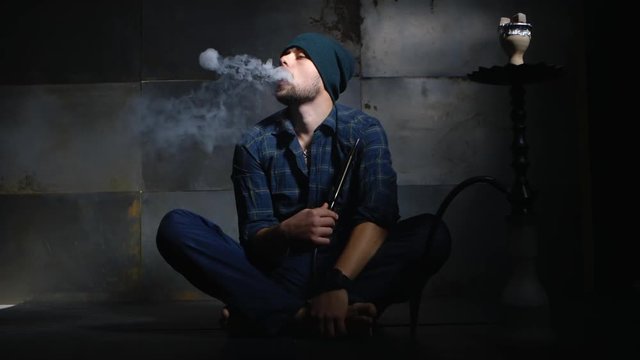 Guy smokes hookah and let smoke rings