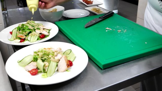 Caesar salad, chef prepares a dish, pouring sauce sliced vegetables, chicken, cherry tomatoes, lettuce, cook prepares professionally on restaurant kitchen