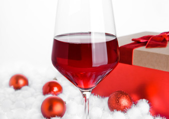 Glass of red wine on snow with christmas balls
