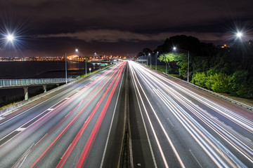 Light trails of cars travelling along the freeway at night with Auckland city in the background