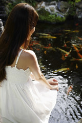 Young woman in white dress sitting by pond