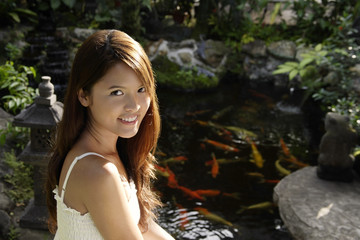 Young woman sitting by koi pond