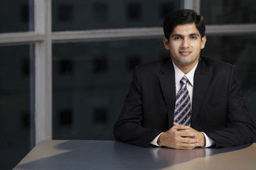 Young man sitting at table hands folded