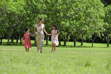 Fototapeta premium Mother and two daughters holding hands, walking across park