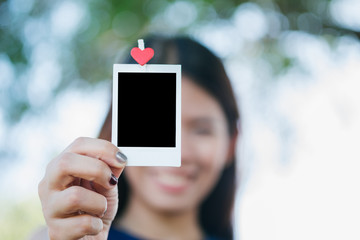 Woman hold  photo instant on hand. Blank instant photo and red clip paper heart. relationship concept.