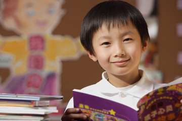Schoolboy with book in hand in class looking at camera