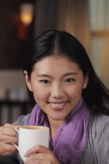 Head shot of young woman holding coffee cup and smiling