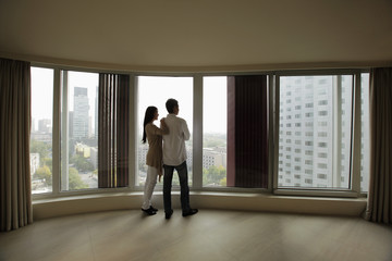 Rear view of young couple looking out large windows of condo