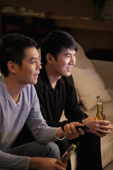Young men watching TV and holding bottles of beer
