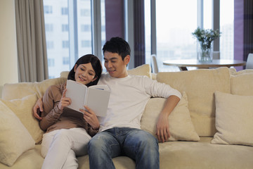 Fototapeta premium Young couple in living room reading a book together