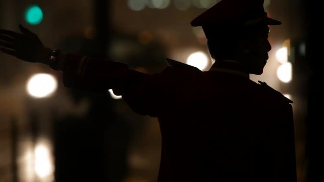 Silhouette of doorman waving down taxi on street at night / Hong Kong, China