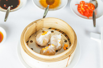Dim sum food Steamed shrimp Fun Goh dumpling in bamboo basket at restaurant with soy sauce, sweet sauce, chili sauce and chopsticks.