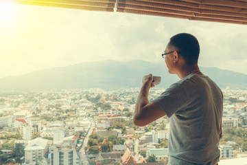 Asian man holding cup of coffee at office he looking out window. Cityscape backdrop. Selective...