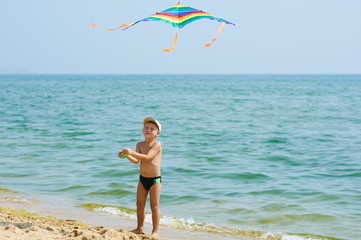 Little boy resting and playing on the beach with a kite