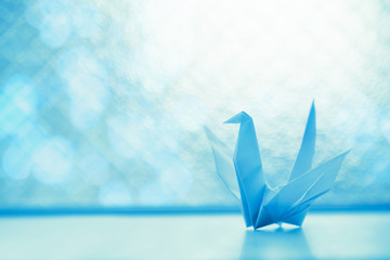 origami paper bird on the bright-lit glass window with blue solf