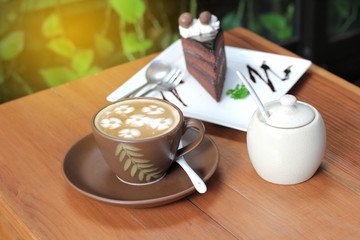  cup of coffee with capucino art and chocolate cake on white plate on the wooden table with vintage filter effect