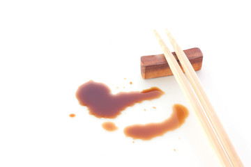 Splashes of soy sauce and chopsticks on white background.