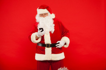Photo of Santa Claus using mobile phone, on a red background. Christmas