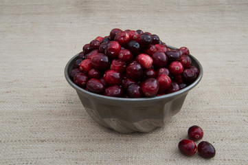 Fresh Red and Maroon Cranberries Heaped in Vintage Metal Food Mold with Beige Woven Cloth Background and Loose Berries in Foreground