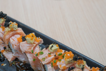 Salmon aburi saikyo sushi on black plate on wooden table