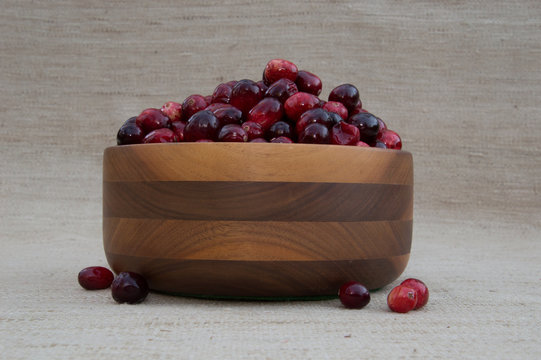 Fresh Red  znd Maroon Cranberries Heaped in Turned Wood Bowl with Berries Out of Dishis Against Beige Woven Fabric Background